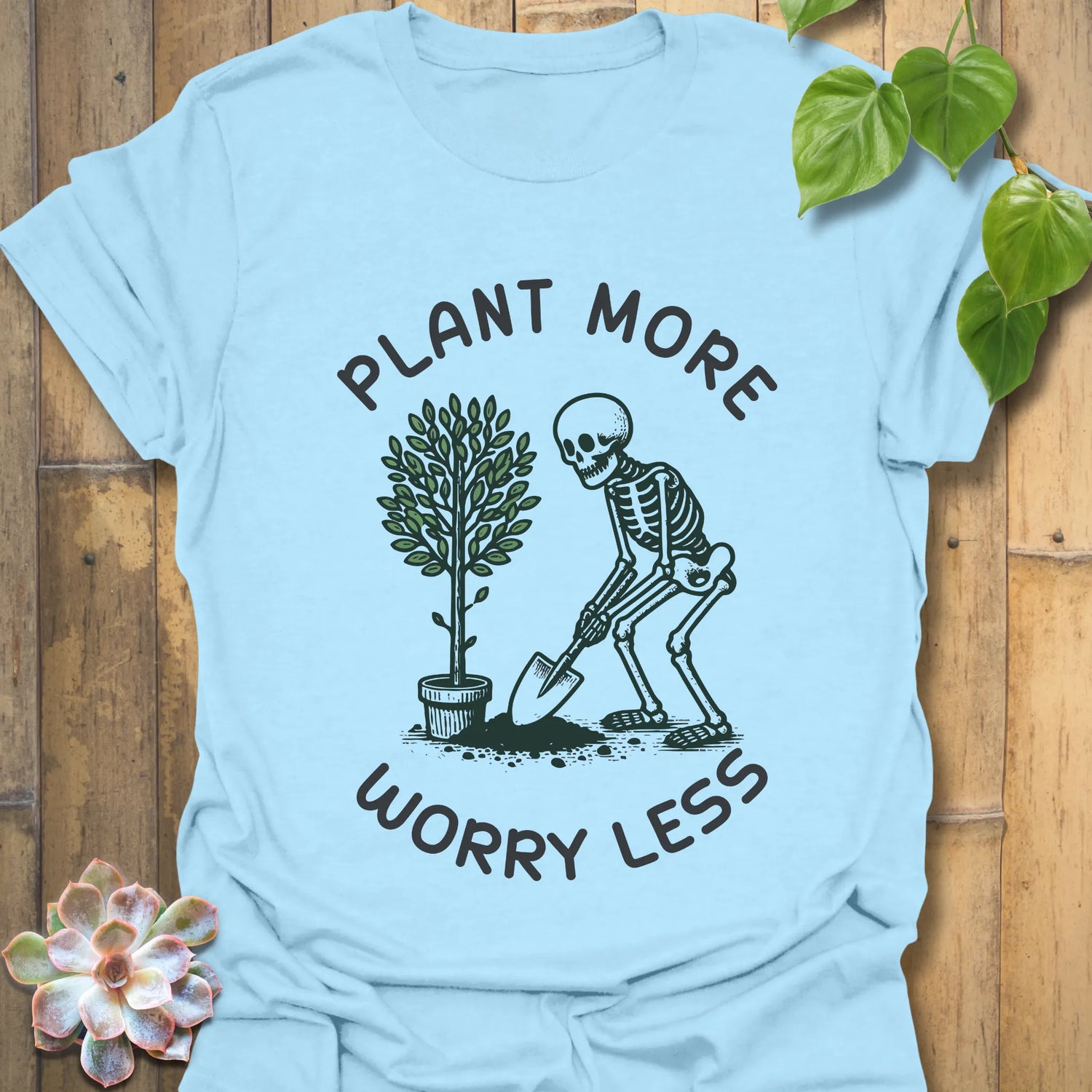 Light blue t-shirt featuring the design Plant More Worry Less with a skeleton and plant character, soft cotton eco-friendly shirt.