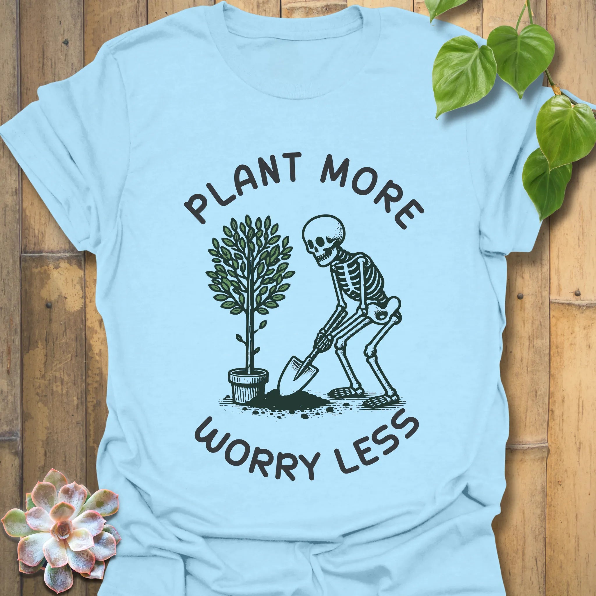 Light blue t-shirt featuring the design Plant More Worry Less with a skeleton and plant character, soft cotton eco-friendly shirt.