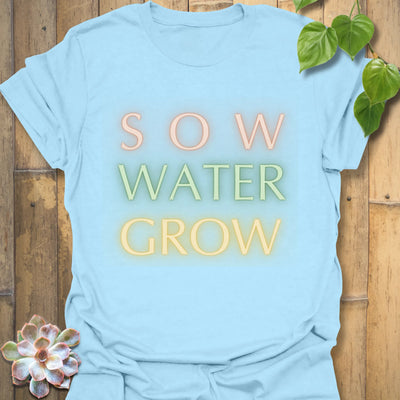 Light blue t-shirt featuring the design Sow Water Grow printed with a botanical watering can illustration.