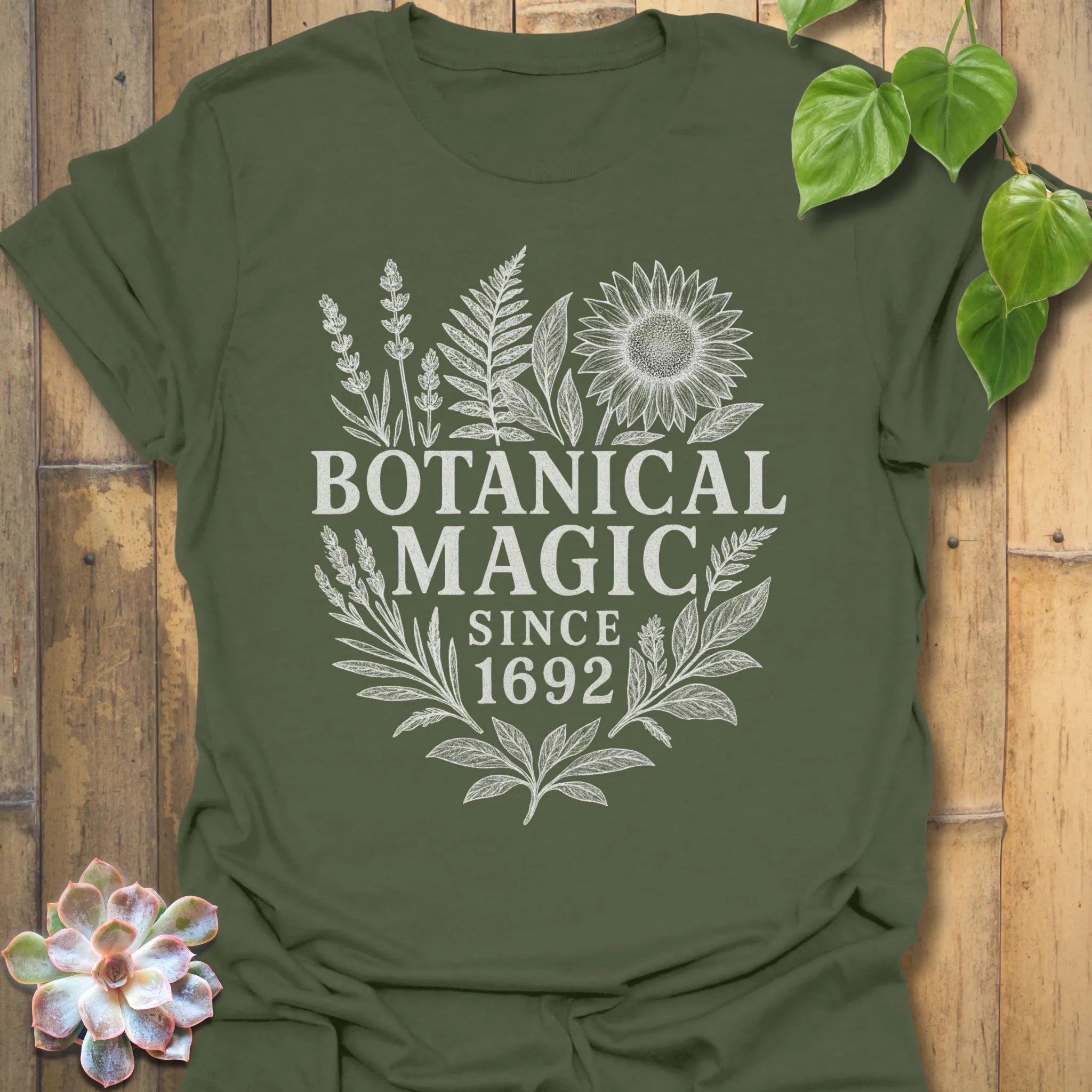Military Green t-shirt featuring the design Botanical Magic printed in bold letters, floral graphic tee.