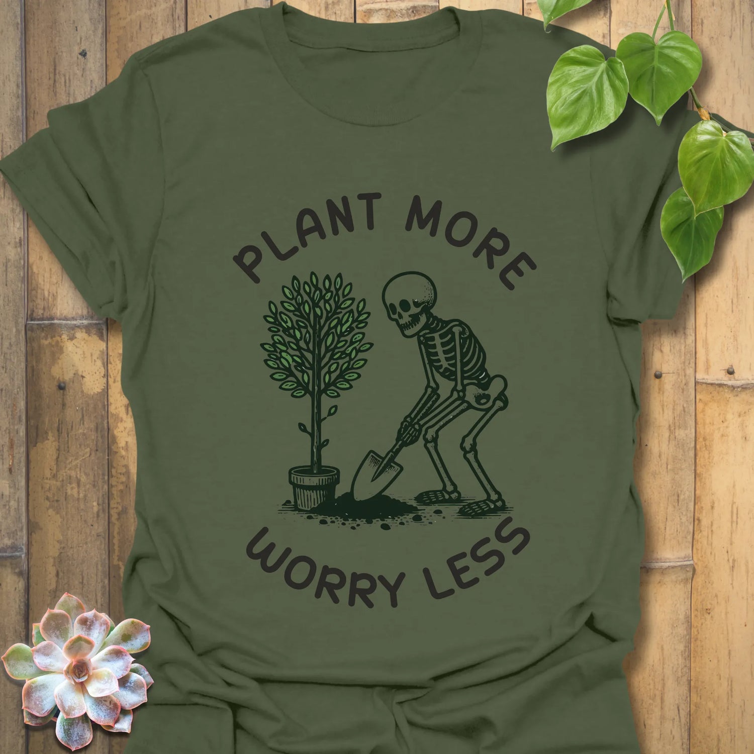Military green t-shirt featuring the design Plant More Worry Less with plants and skeleton illustration, nature-inspired eco graphic tee.