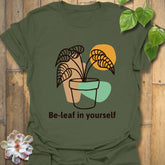 Military green t-shirt featuring the phrase “Be-leaf in yourself” with a potted plant graphic