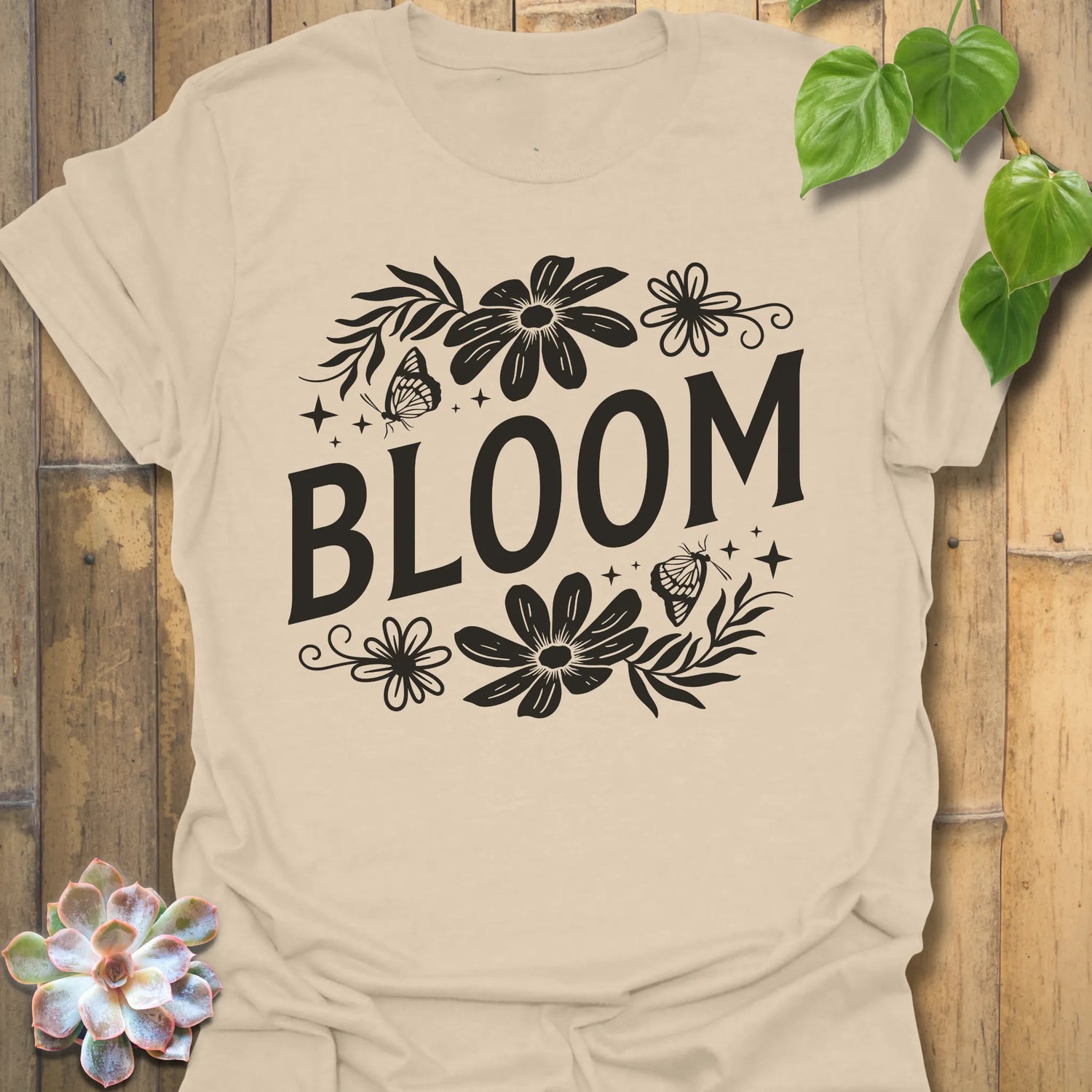 Sand t-shirt featuring the design Bloom printed in bold black letters, floral graphic tee for plant lovers.