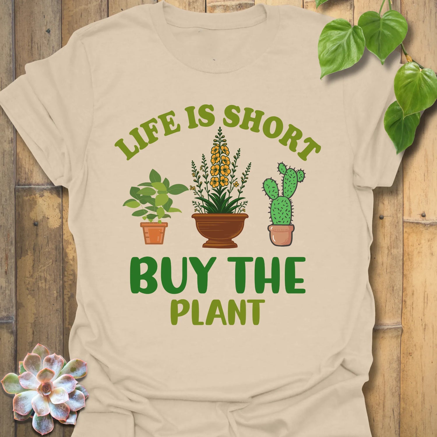 Sand t-shirt featuring the design Buy The Plant printed in bold letters, funny gardening shirt.
