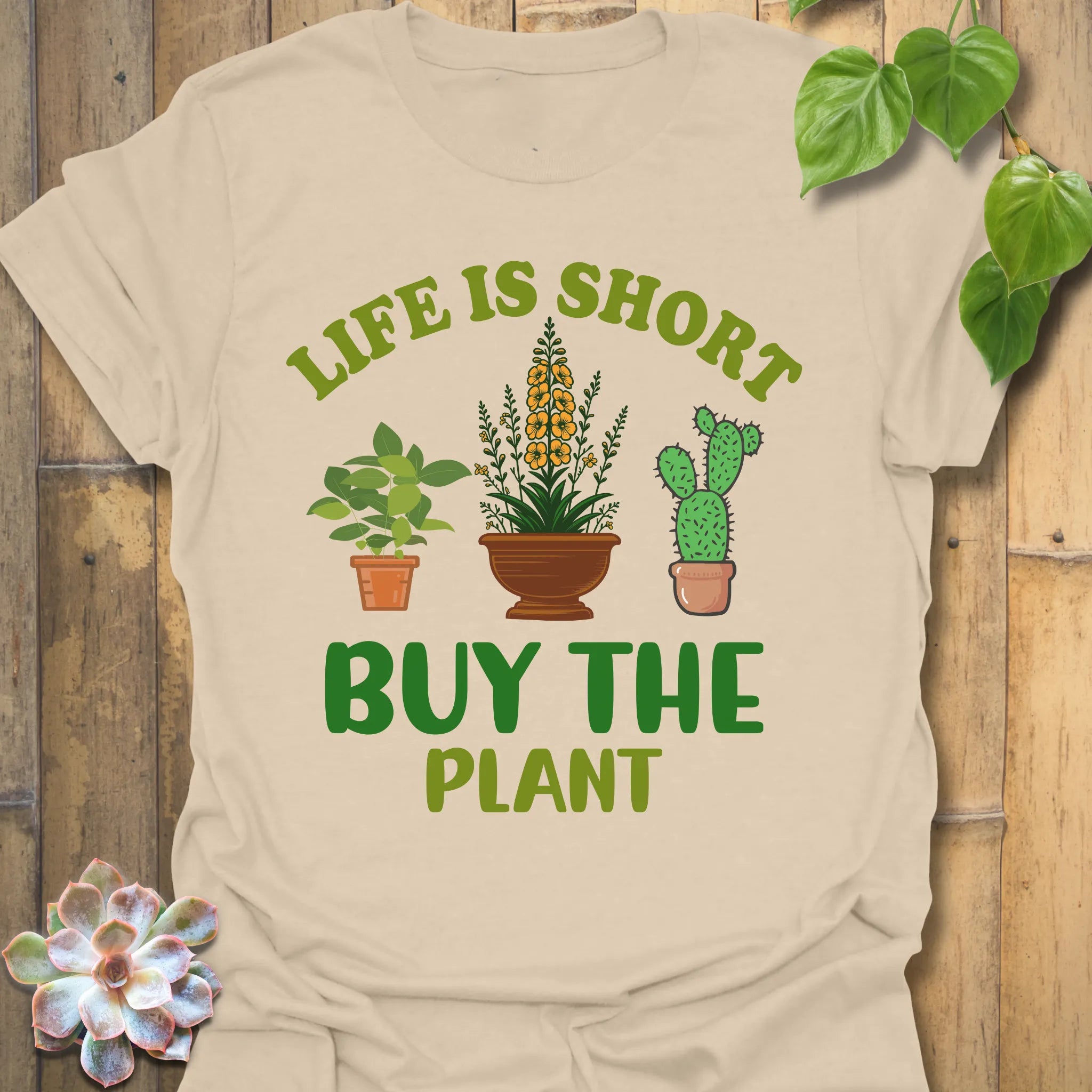 Sand t-shirt featuring the design Buy The Plant printed in bold letters, funny gardening shirt.