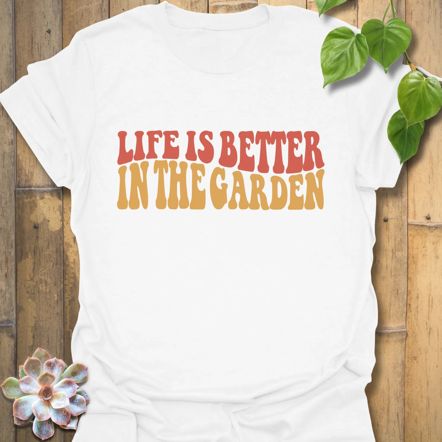 White t-shirt featuring the design Life is better in the garden printed in green floral lettering, perfect gardening shirt for plant lovers.