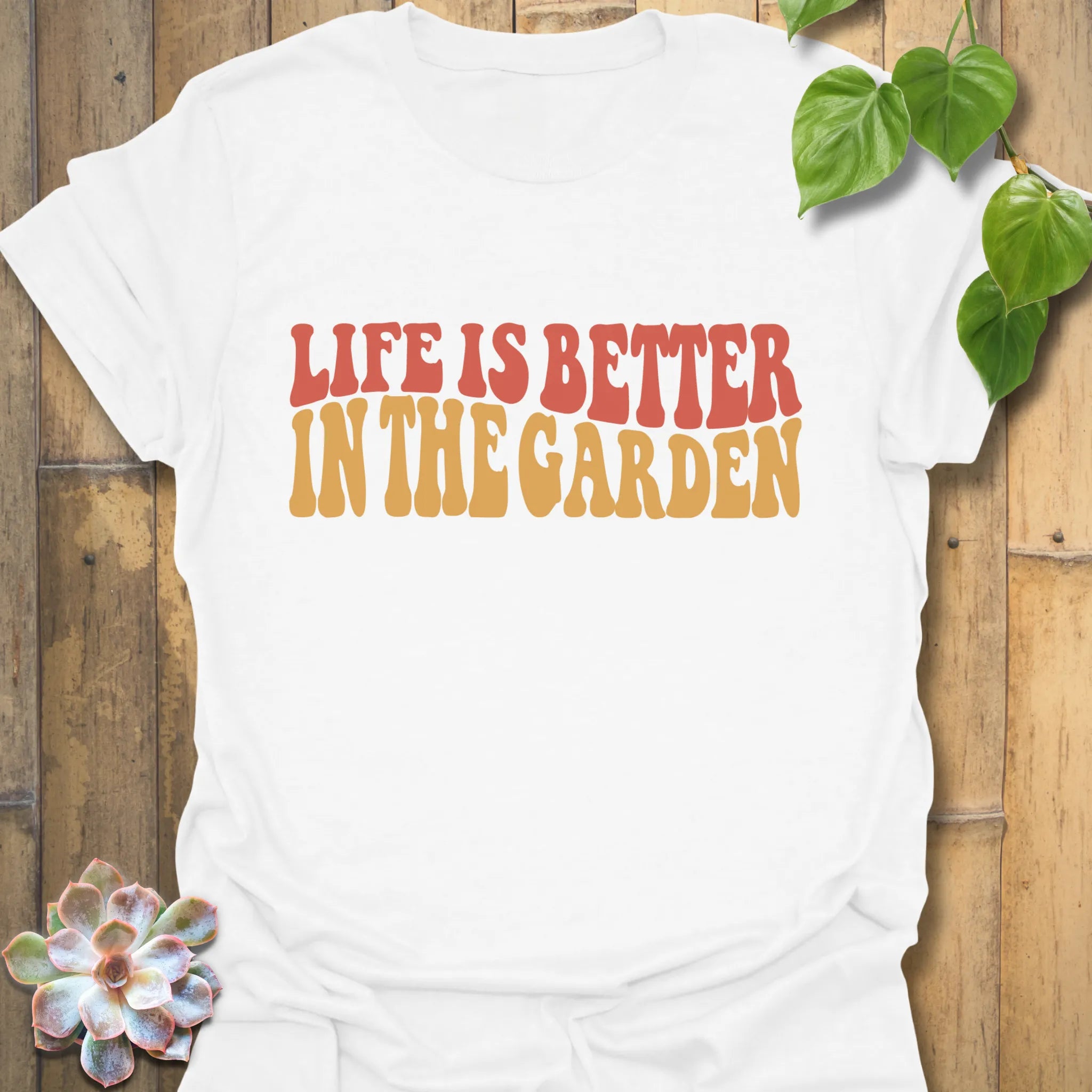 White t-shirt featuring the design Life is better in the garden printed in green floral lettering, perfect gardening shirt for plant lovers.