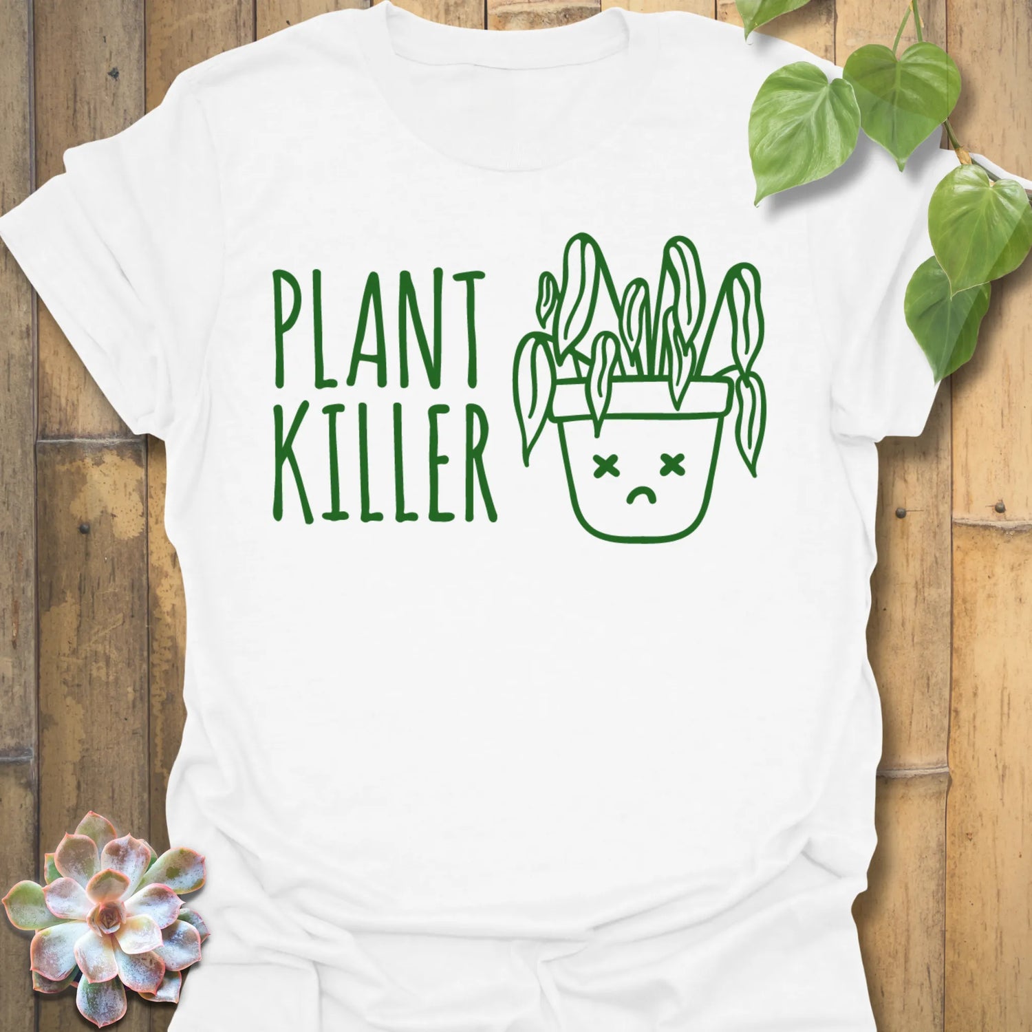 White t-shirt featuring the design Plant Killer printed in bold green letters, funny plant lover shirt.